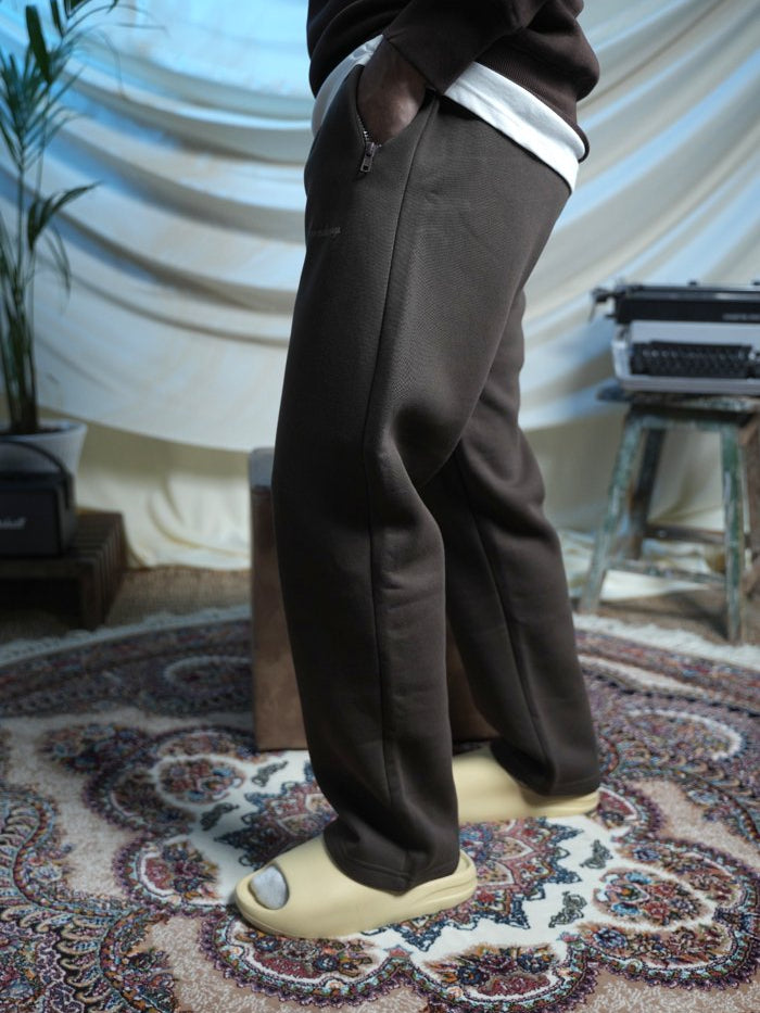 Person wearing brown pants and white shoes on a patterned rug with a draped curtain background