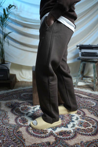 Person wearing brown pants and white shoes on a patterned rug with a draped curtain background