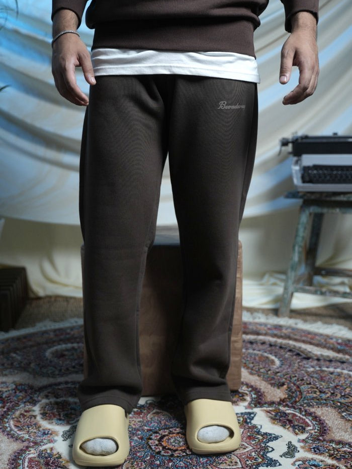 Person wearing brown pants with a logo, standing on a patterned rug.