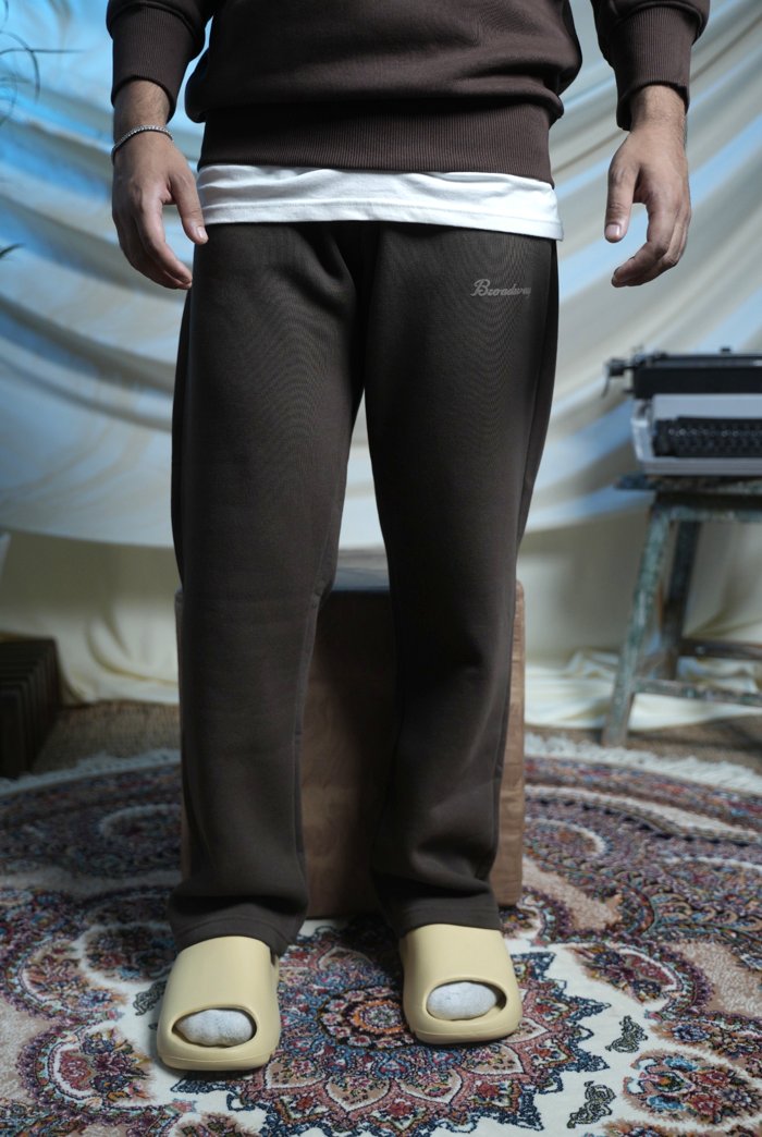 Person wearing brown pants with a logo, standing on a patterned rug.